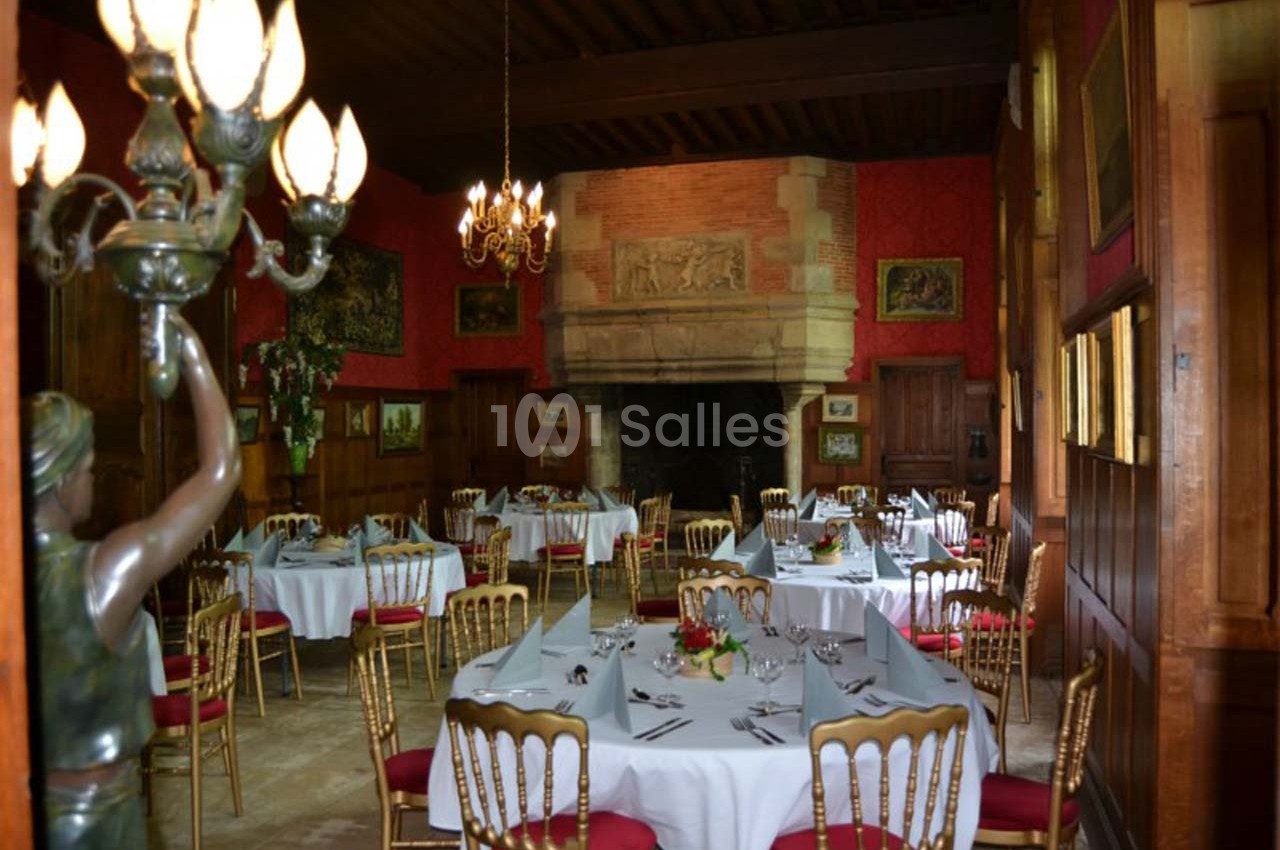 Salle de restaurant élégante avec tables dressées, chaises dorées et cheminée en pierre dans un décor classique.