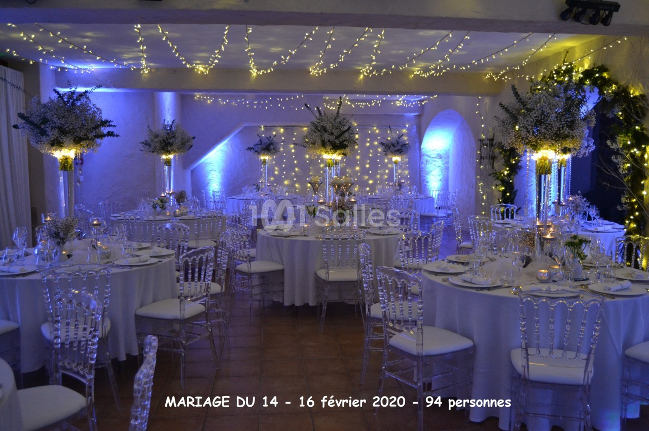 Salle de réception décorée pour un mariage, avec tables rondes, chaises transparentes et éclairage tamisé.