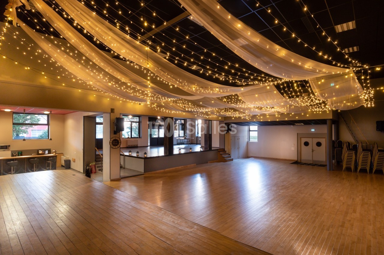 Salle spacieuse avec parquet, rideaux lumineux suspendus et espace aménagé pour des événements ou activités.