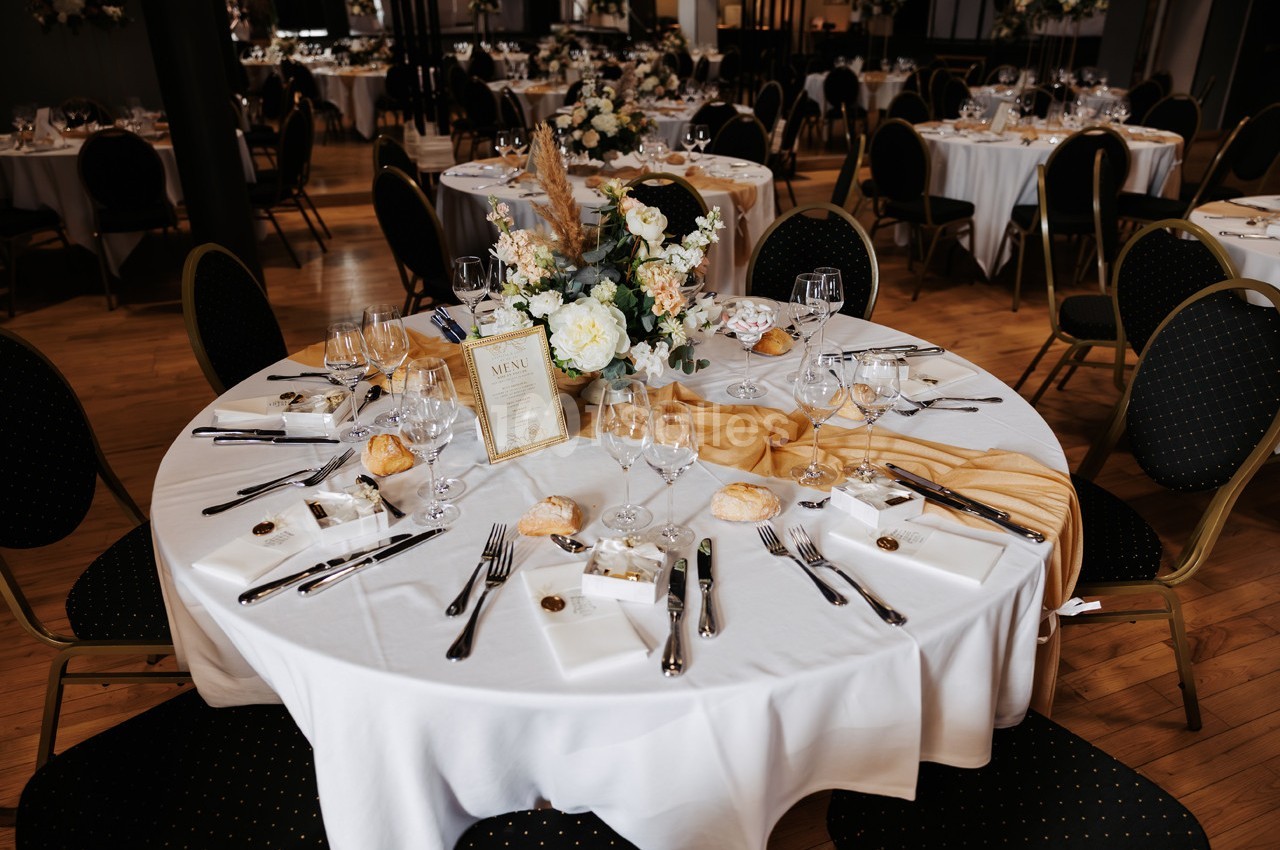Table élégamment dressée avec nappes blanches, couverts, fleurs et menu, dans une salle de réception.