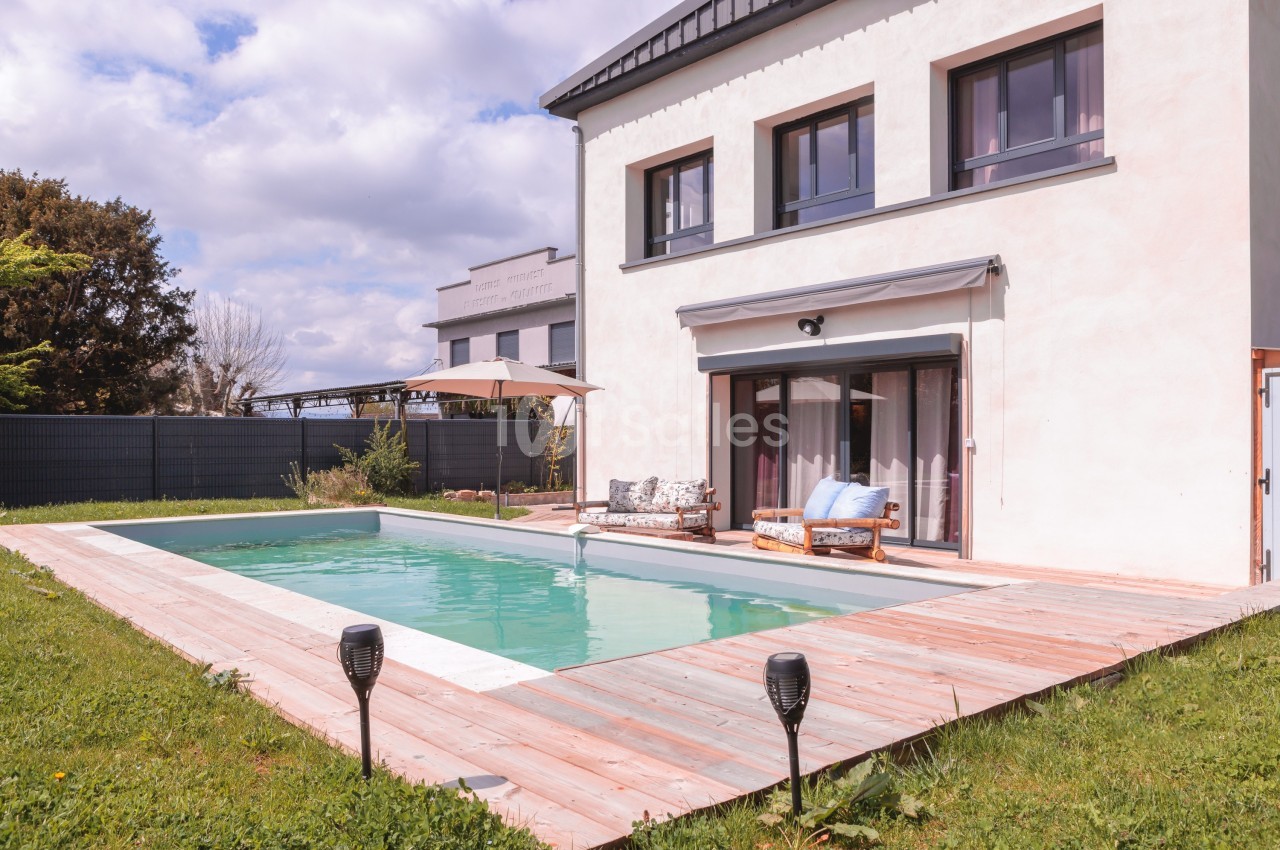 Maison moderne avec piscine extérieure entourée d'une terrasse en bois, jardin et mobilier de détente.