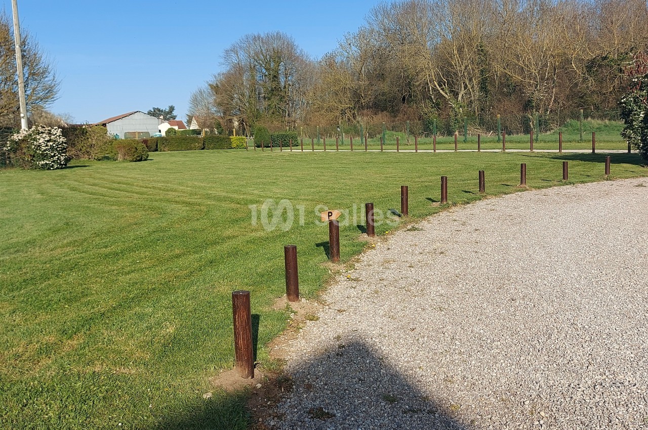Pelouse bien entretenue bordée de poteaux en bois, avec un chemin gravillonné et des arbres en arrière-plan.