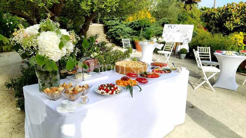 Buffet en plein air avec table garnie de plats variés, entourée de chaises blanches et végétation luxuriante.