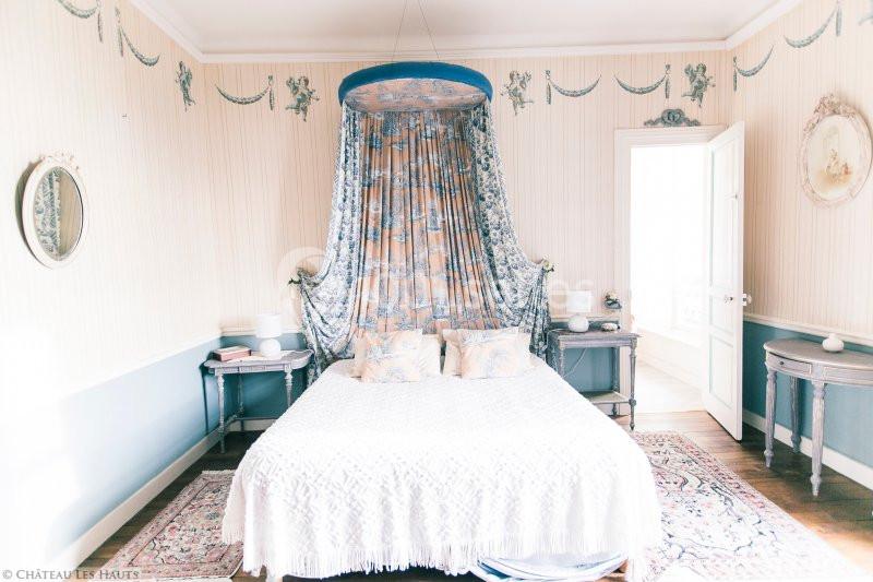 Chambre lumineuse avec lit à baldaquin, décorée de motifs classiques, murs clairs et mobilier ancien.