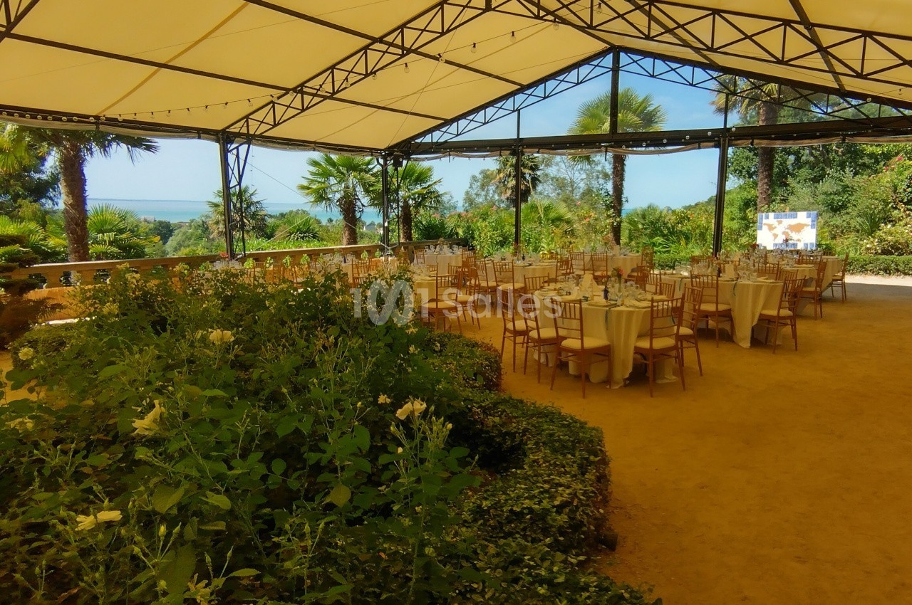 Salle extérieure couverte avec des tables dressées pour un événement, entourée de verdure et offrant une vue dégagée.