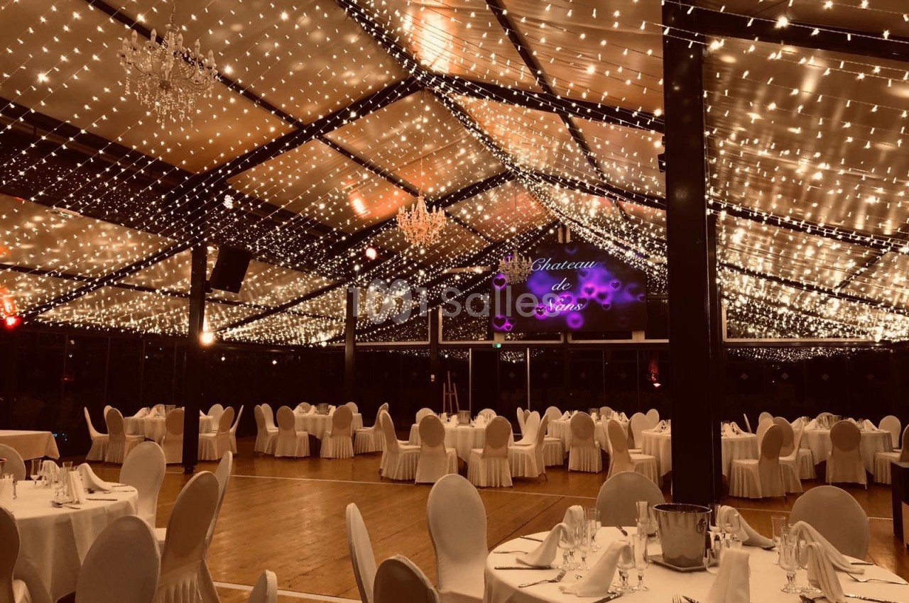 Salle de réception élégamment décorée avec des guirlandes lumineuses suspendues et des tables dressées.