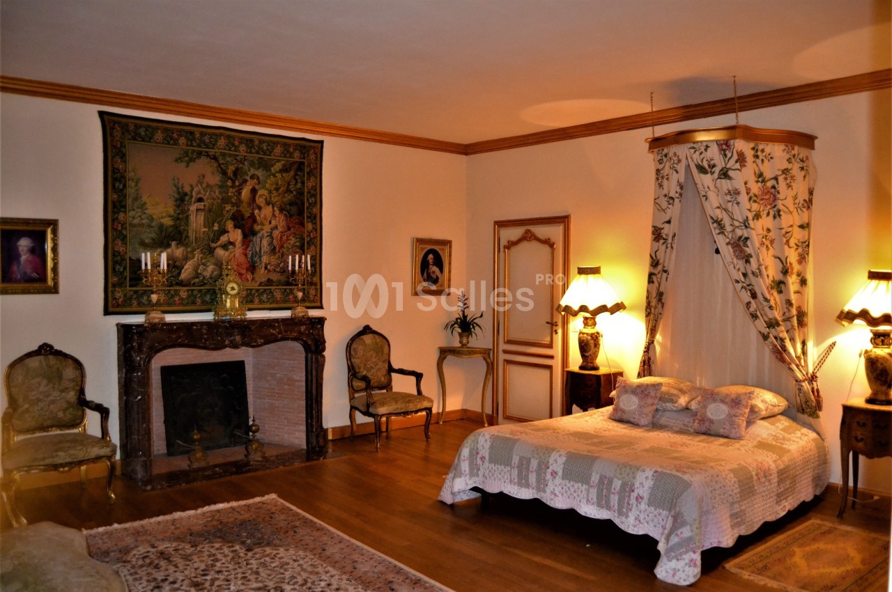 Chambre élégante avec lit à baldaquin, cheminée ornée, tapis et mobilier ancien dans un décor chaleureux.