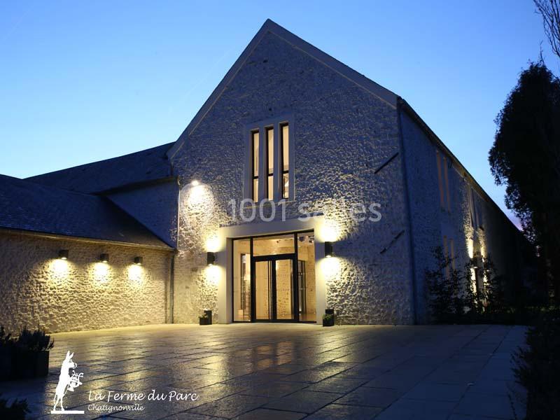 Façade éclairée d'un bâtiment en pierre avec une grande entrée vitrée, photographiée à la tombée de la nuit.