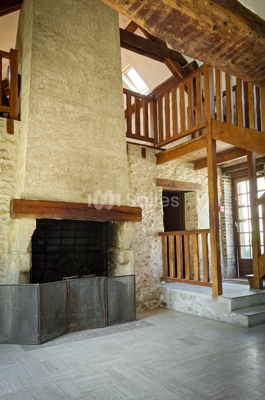 Cheminée en pierre dans un intérieur rustique avec mezzanine en bois et poutres apparentes.
