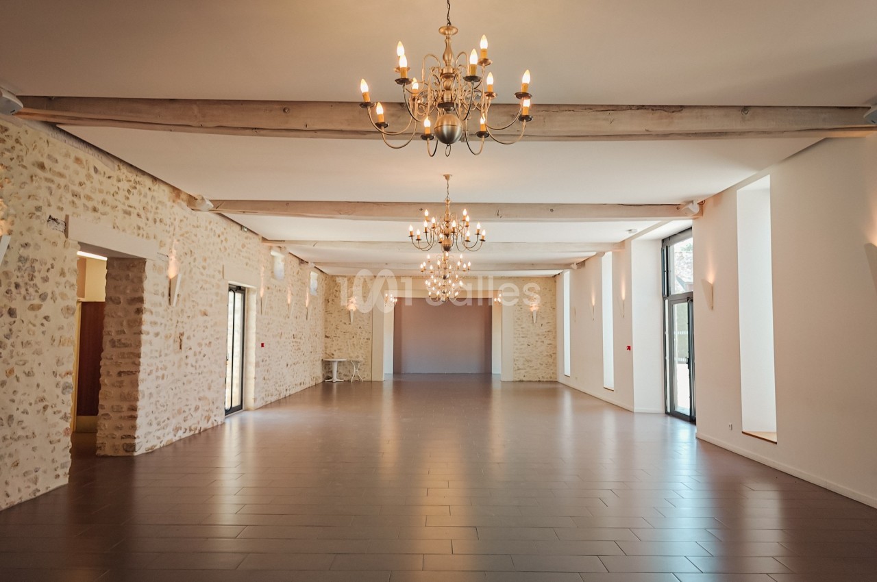Salle spacieuse avec murs en pierre, parquet sombre, poutres apparentes et lustres suspendus.