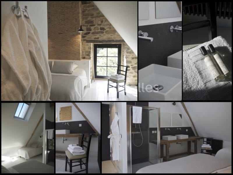 Chambre mansardée avec murs en pierre, lit, salle de bain moderne, serviettes, produits de toilette et lumière naturelle.