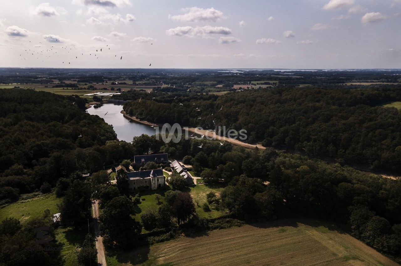 Vue aérienne d'un paysage rural avec une rivière sinueuse, une forêt dense et un bâtiment entouré de verdure.