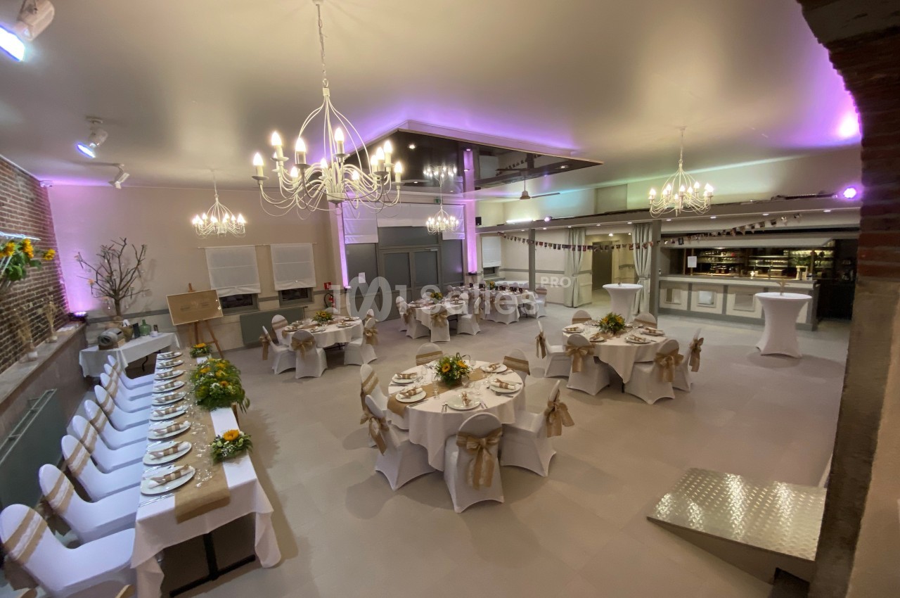 Salle de réception décorée avec des tables rondes dressées, des chaises ornées de nœuds et un éclairage tamisé.