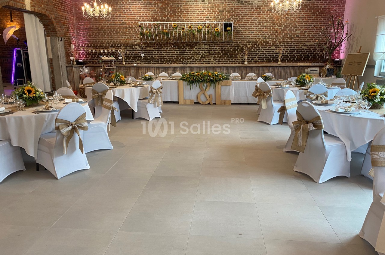 Salle de réception décorée avec des tables rondes, nappes blanches, chaises ornées de rubans et des tournesols en centre de…