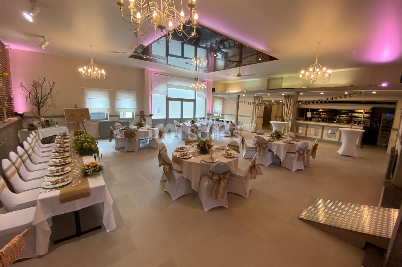 Salle de réception décorée avec des tables rondes dressées, des chaises blanches et un éclairage tamisé.