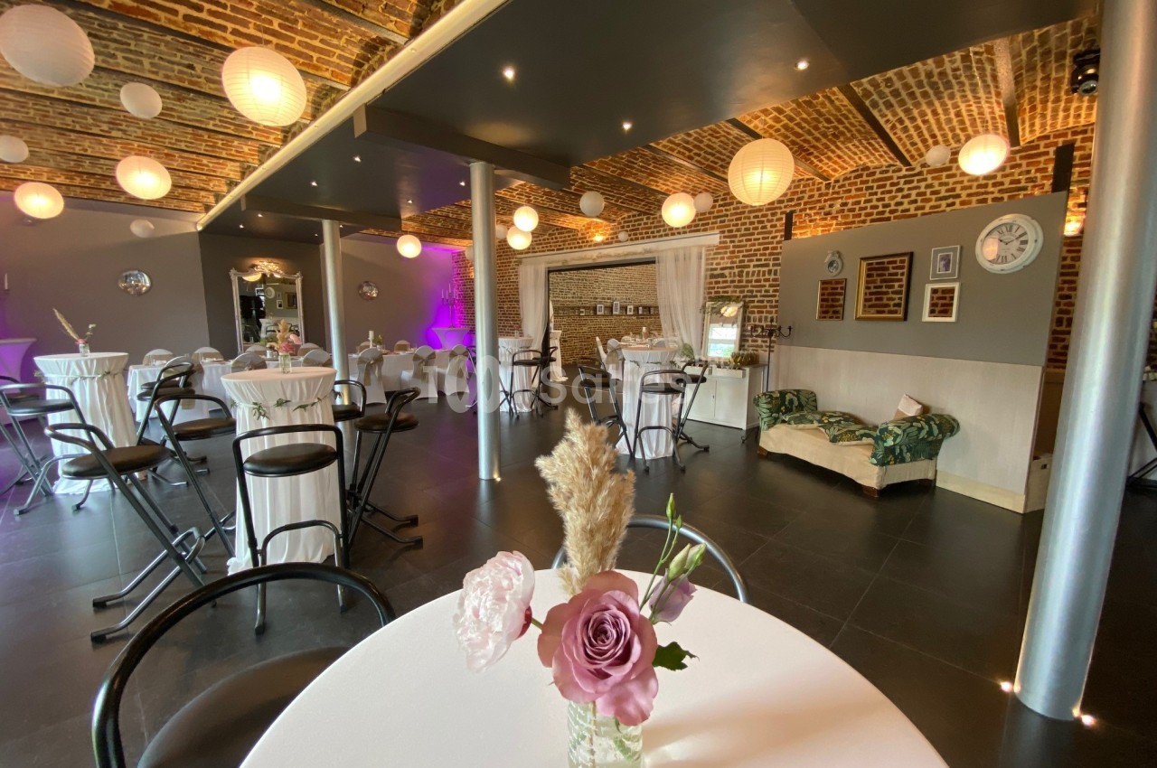 Salle de réception avec murs en briques, tables hautes décorées et éclairage tamisé, ambiance conviviale.