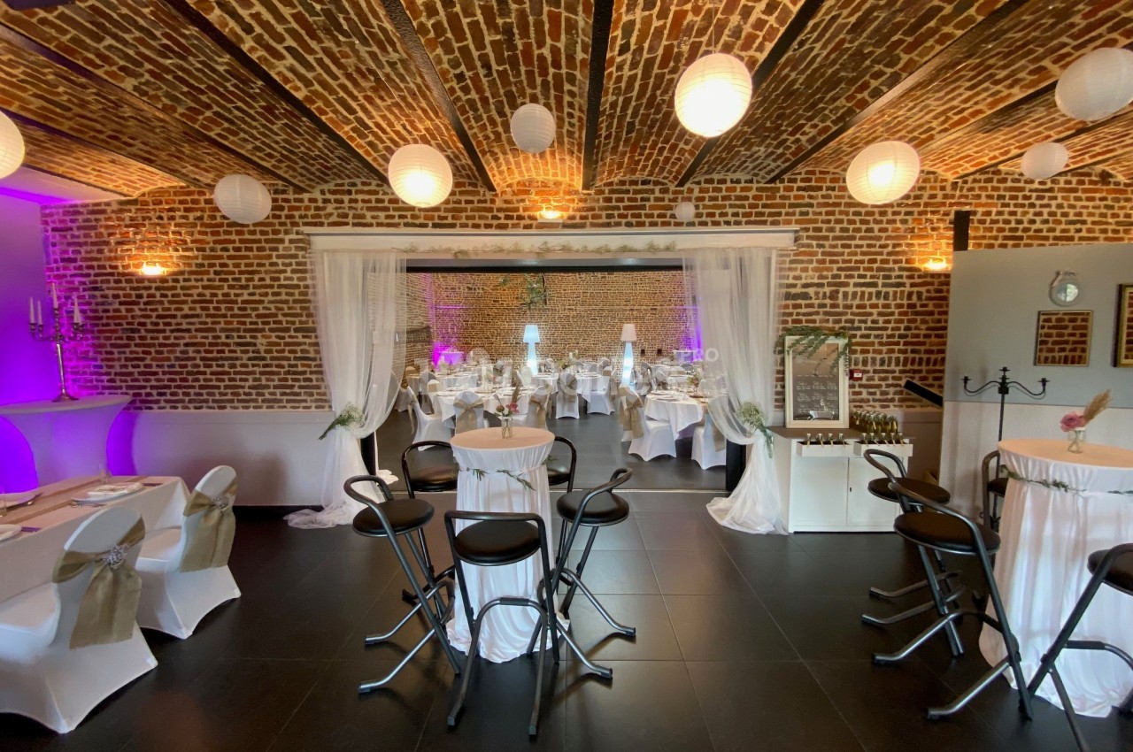 Salle de réception avec murs en briques, tables décorées et éclairage tamisé, ambiance chaleureuse et festive.