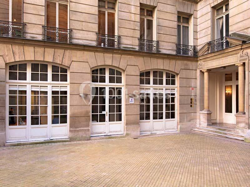 Façade d'un bâtiment en pierre avec grandes fenêtres et une cour pavée.