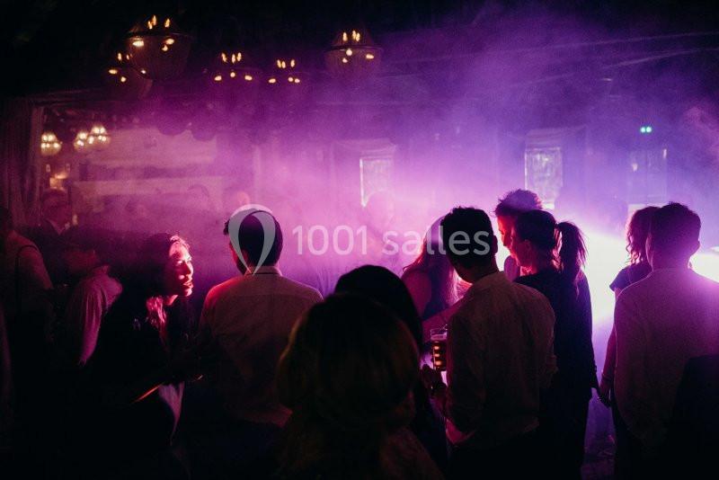 Des personnes discutent et dansent dans une ambiance tamisée avec des lumières violettes et des ombres.