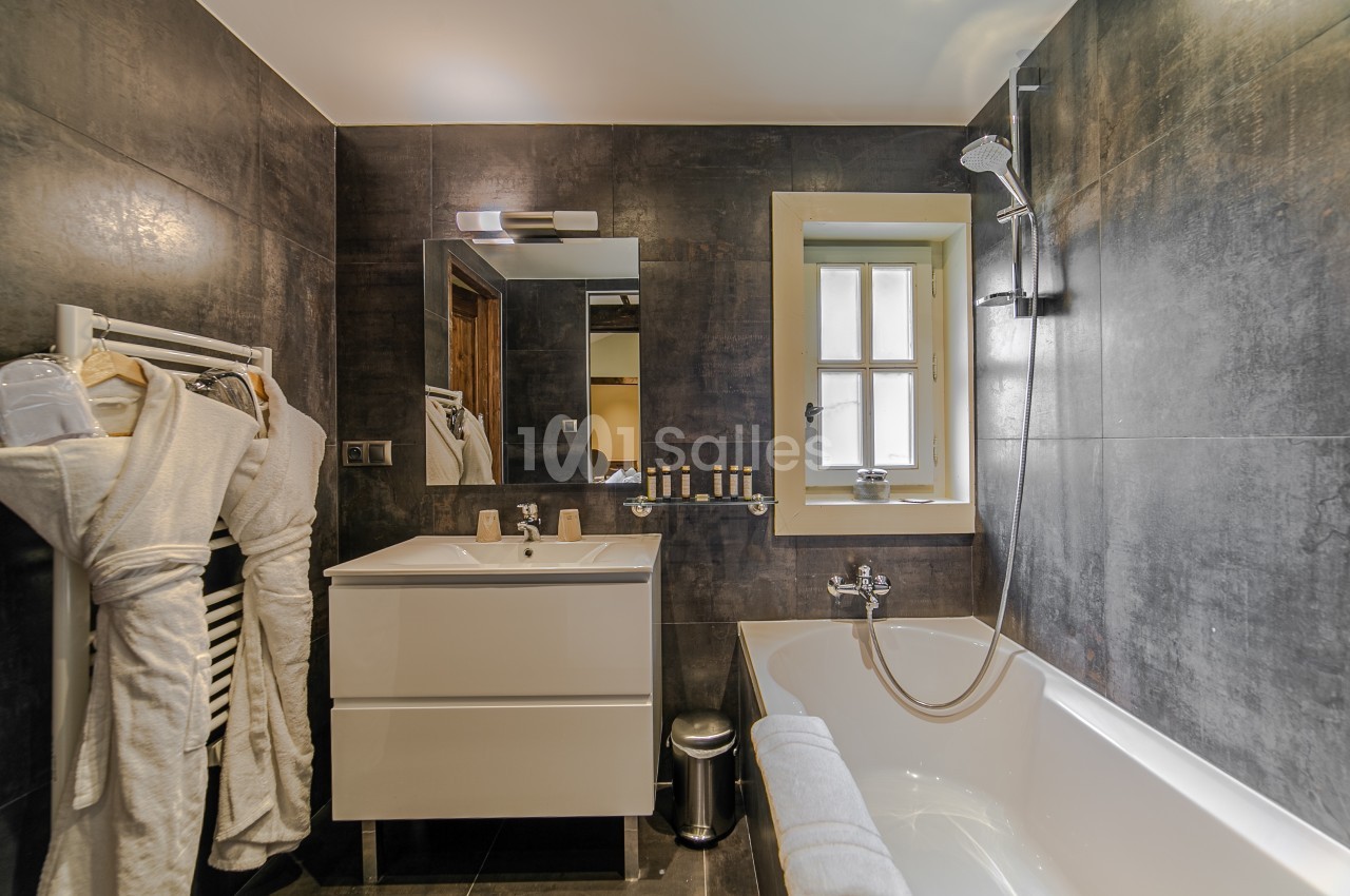 Salle de bain moderne avec baignoire, meuble lavabo, miroir, porte-serviettes et murs en carrelage sombre.