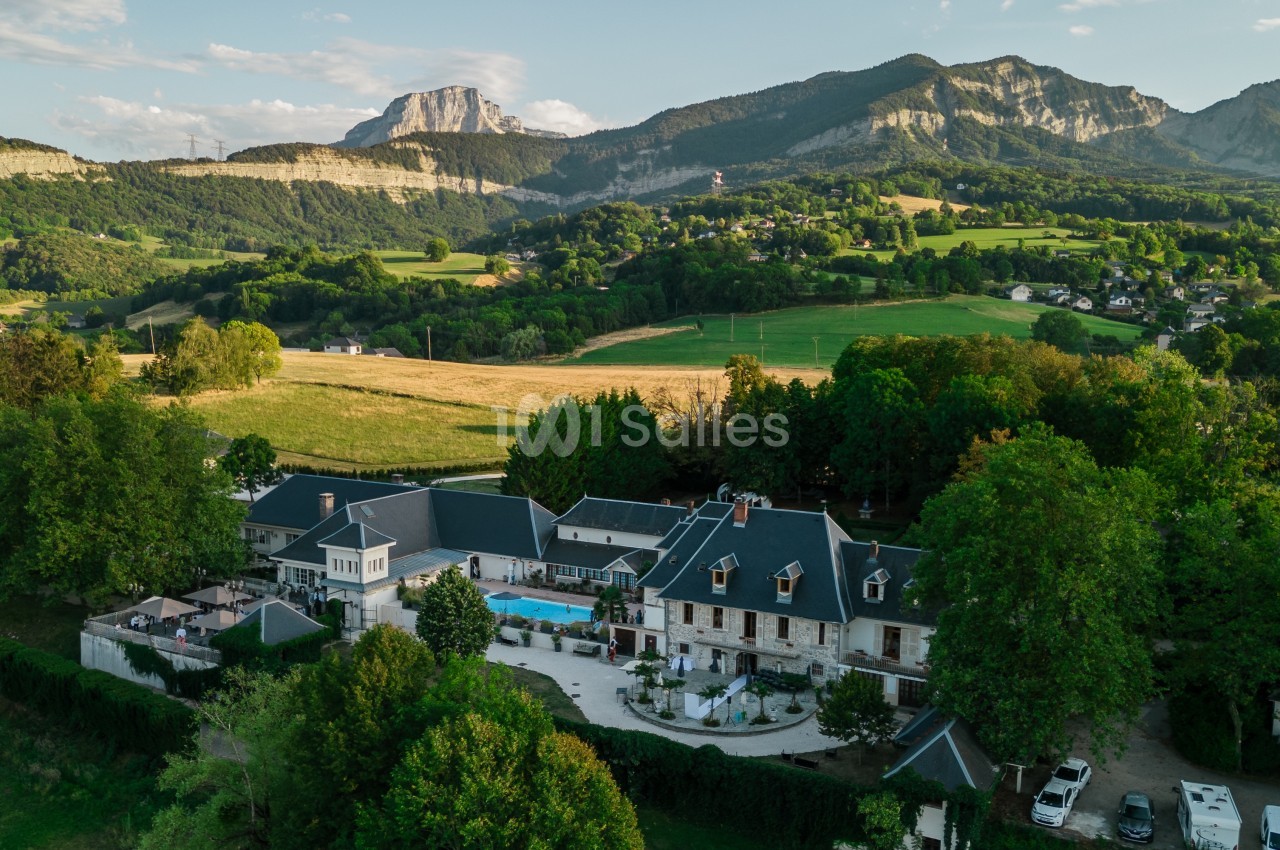 Vue aérienne d'un domaine entouré de verdure, avec des montagnes en arrière-plan sous un ciel dégagé.