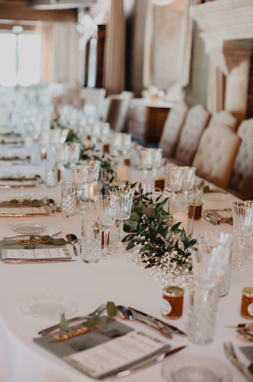 Table élégamment dressée avec nappes blanches, verres en cristal, menus et décoration florale.