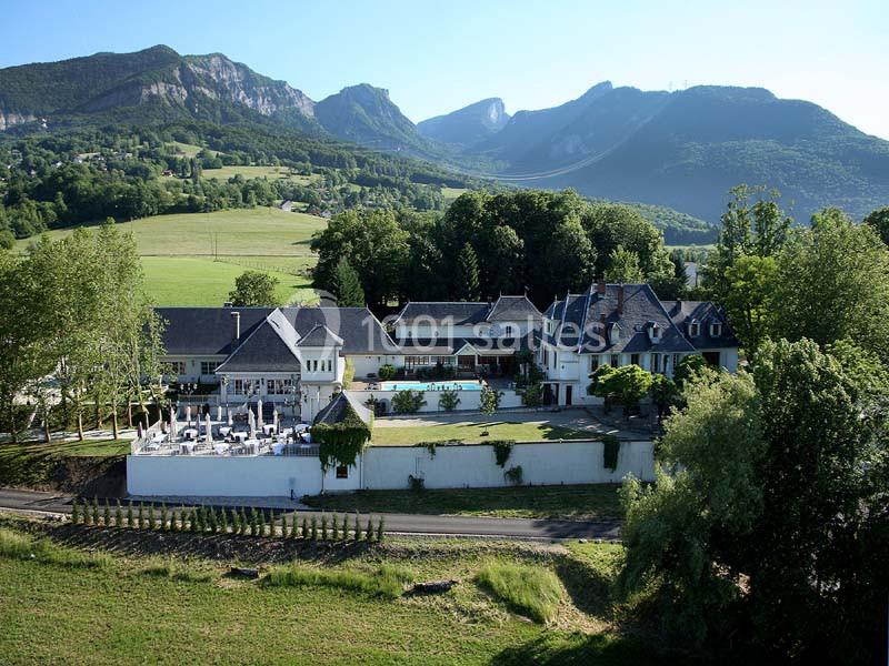 Vue aérienne d'un domaine avec bâtiments traditionnels, terrasse et vignoble, entouré de montagnes et de verdure.