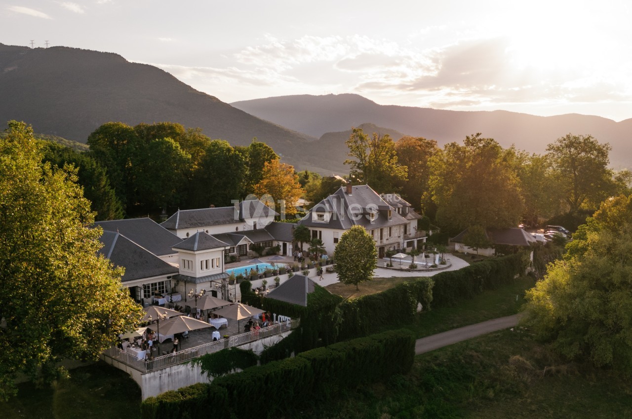 Vue aérienne d'un domaine entouré de verdure avec une piscine, des terrasses et des montagnes en arrière-plan au coucher du…