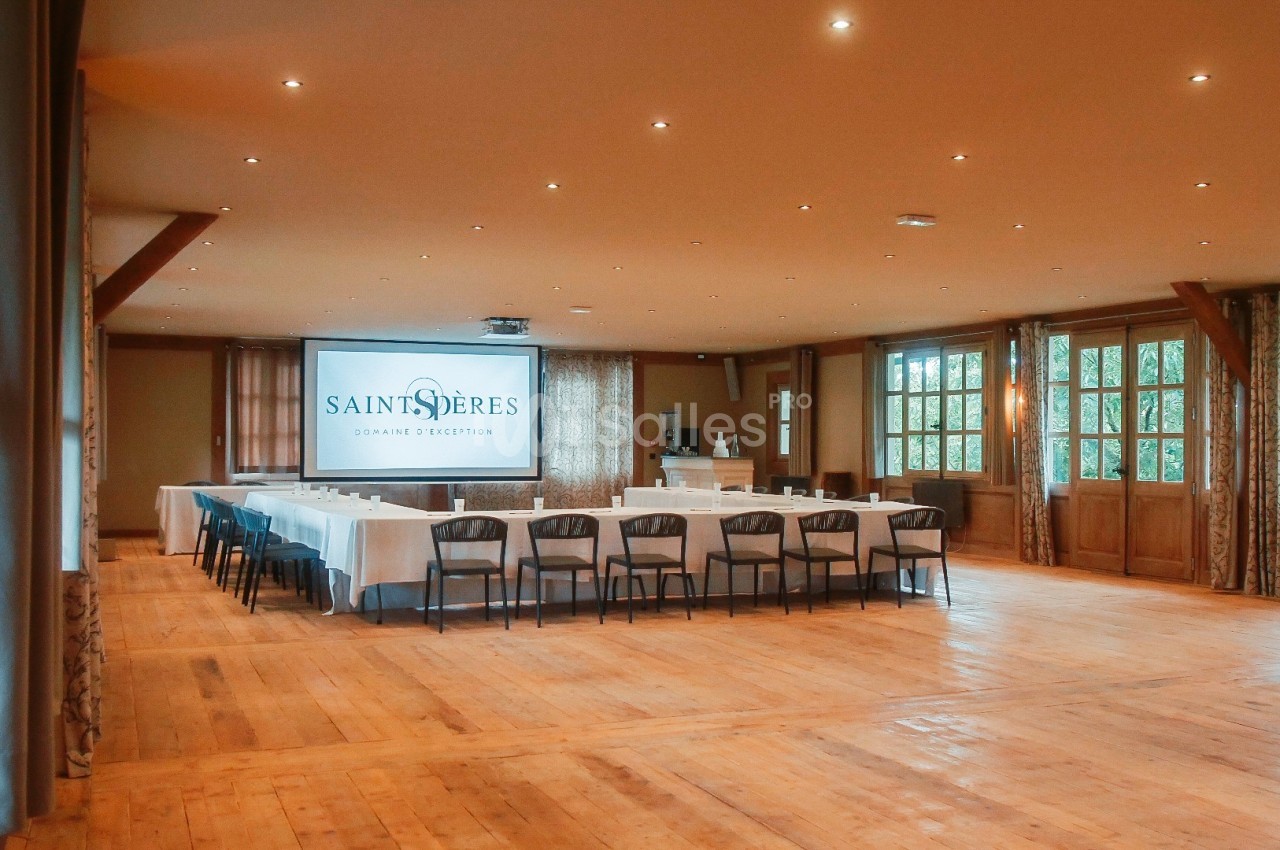Salle de réunion lumineuse avec tables disposées en U, écran de projection et grandes fenêtres donnant sur l'extérieur.