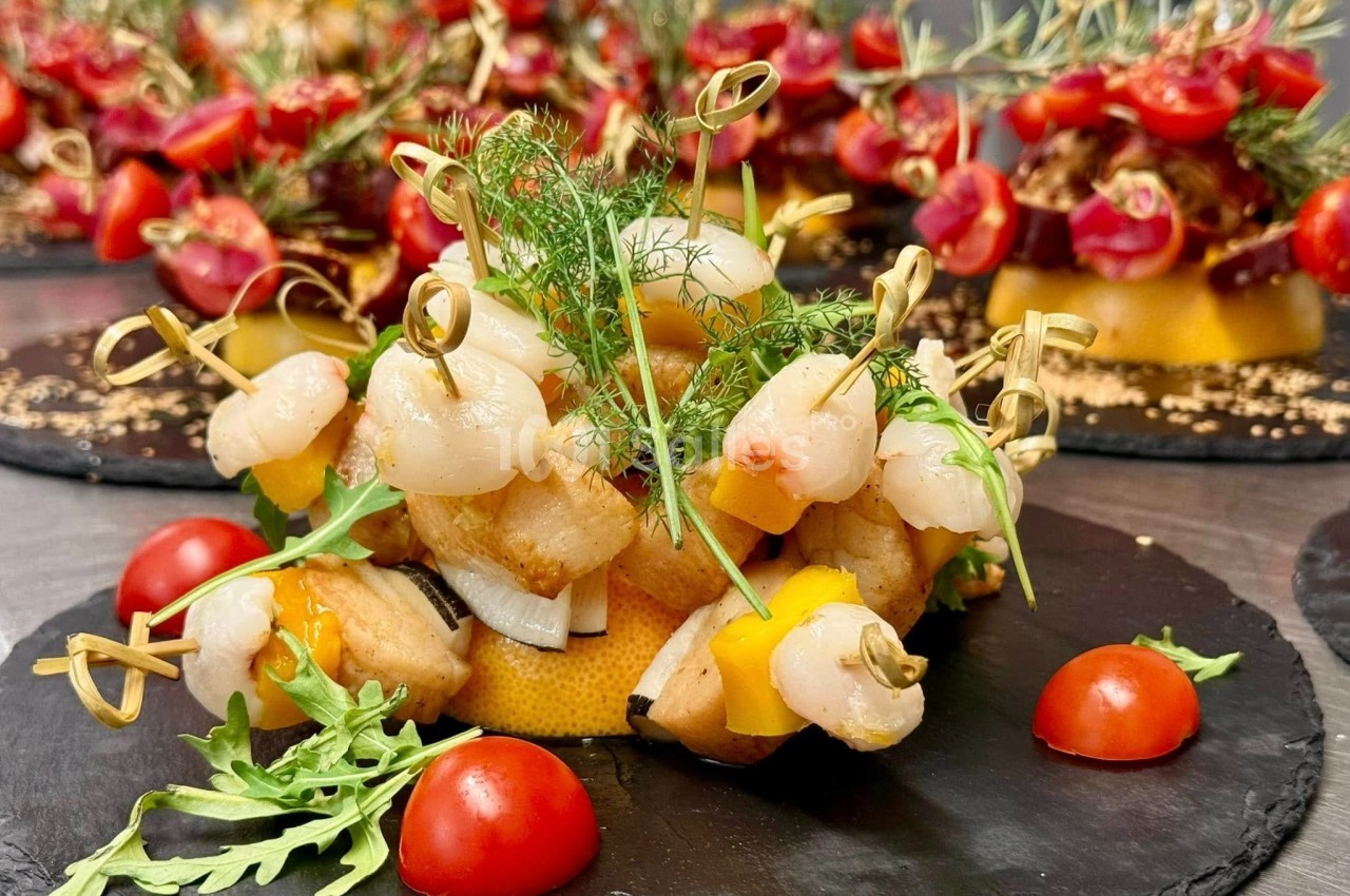 Brochettes de fruits de mer garnies de légumes, servies sur une assiette ardoise avec tomates cerises et roquette.
