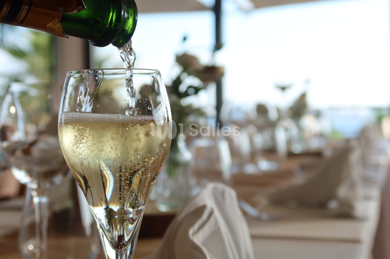 Un verre de champagne est rempli sur une table élégamment dressée avec des serviettes et des fleurs en arrière-plan.