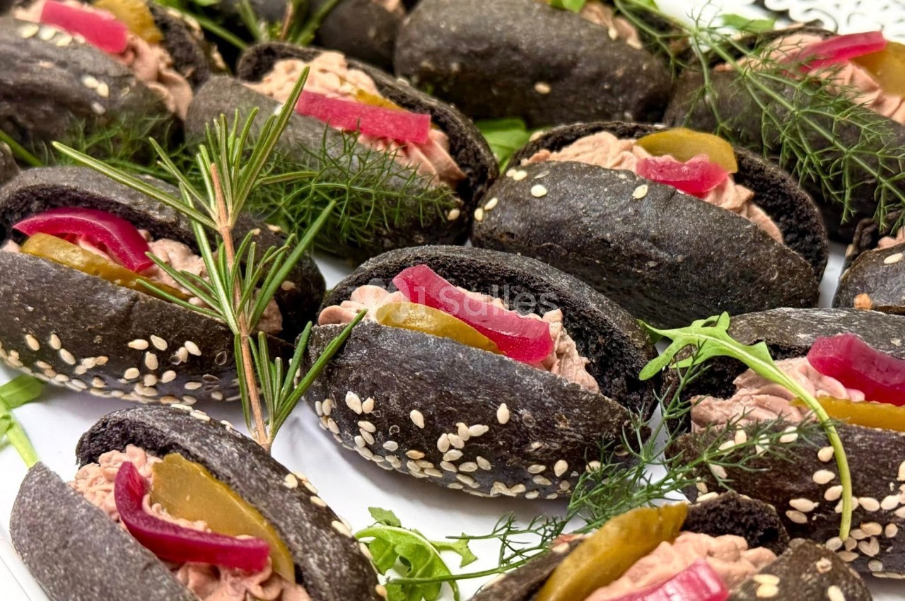 Mini pains noirs garnis de pâté, cornichons, oignons rouges marinés, herbes fraîches et graines de sésame.