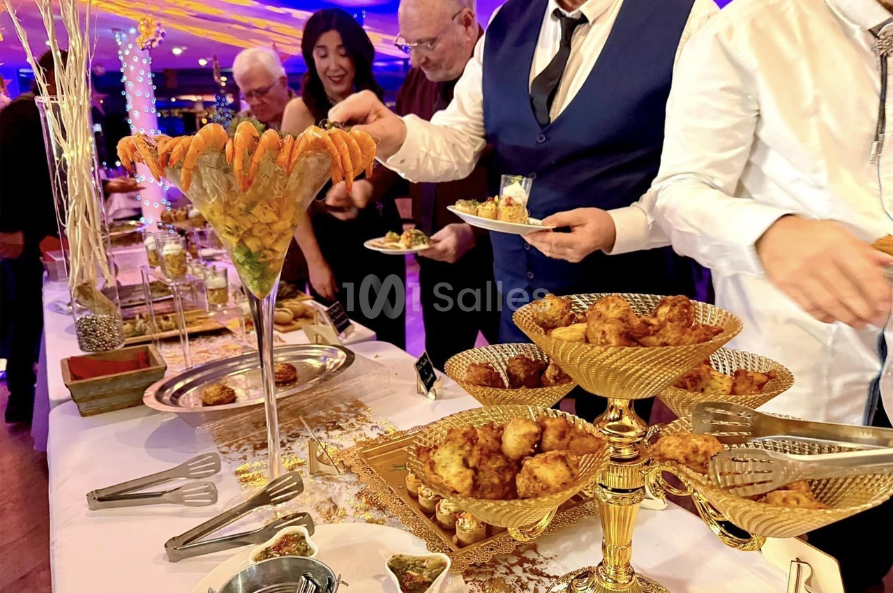 Buffet élégant avec verrines de crevettes et assortiments de bouchées dorées, des convives se servant.