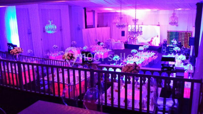 Salle de réception décorée avec des tables dressées, éclairage coloré et ambiance festive.