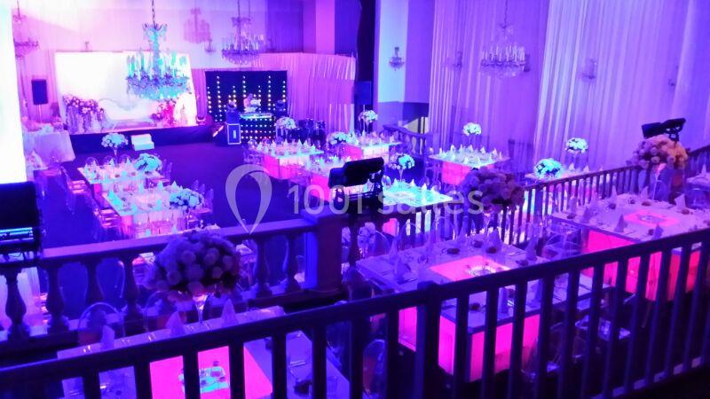 Salle de réception décorée avec des tables illuminées, des fleurs et un éclairage violet pour un événement festif.
