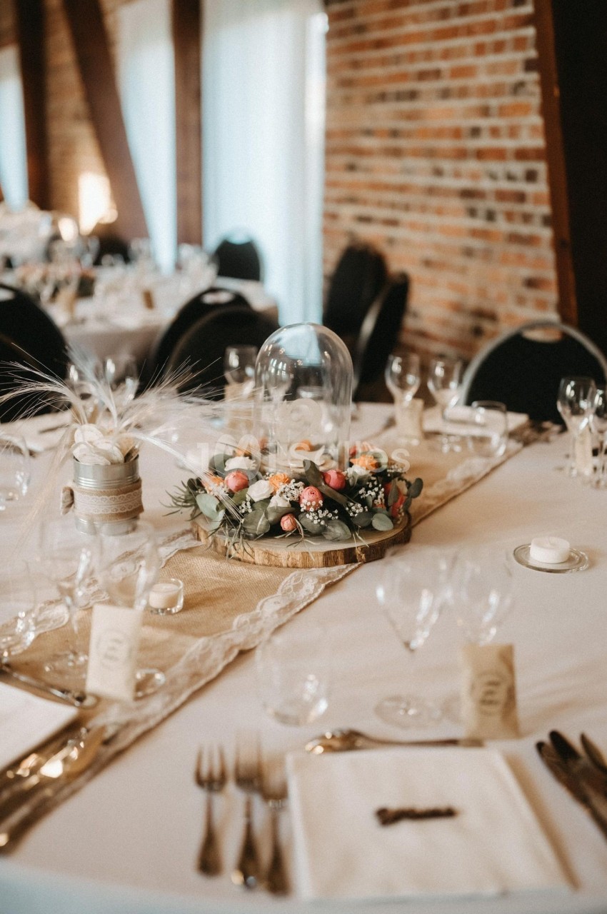 Table décorée pour un événement avec centre de table floral sous cloche en verre, nappes beige et vaisselle élégante.