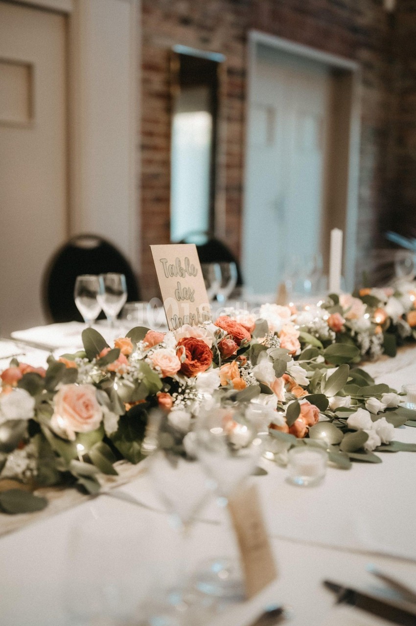 Décoration de table avec un centre de table floral composé de roses et feuillage, dans une salle aux murs en briques.
