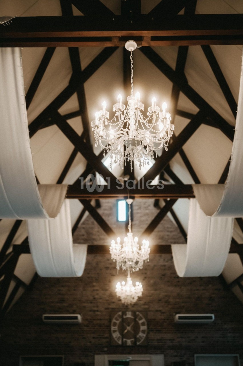 Plafond avec poutres apparentes, lustres en cristal allumés et drapés blancs suspendus dans une salle élégante.