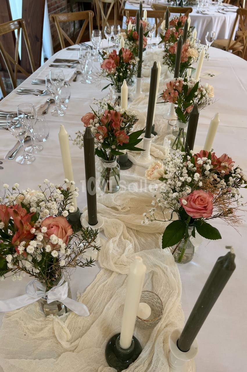 Table décorée avec des bougies, nappes blanches, petits bouquets de fleurs roses et blanches dans des vases en verre.