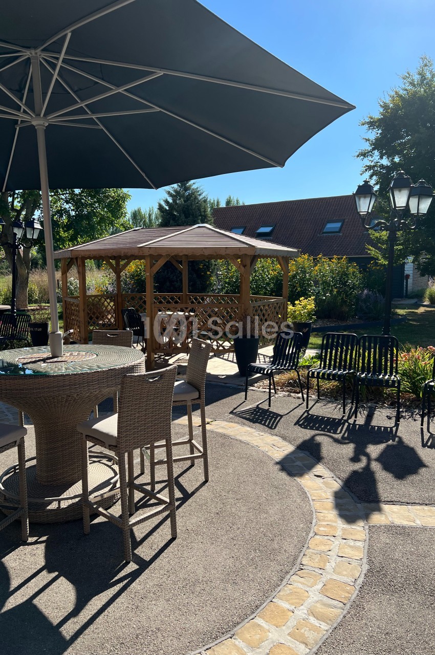 Terrasse ensoleillée avec table, chaises, parasol et pergola en bois dans un jardin verdoyant.