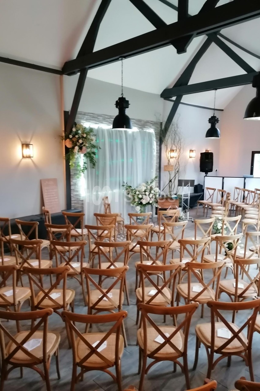Salle de réception décorée pour une cérémonie, avec des chaises en bois disposées face à une arche fleurie.
