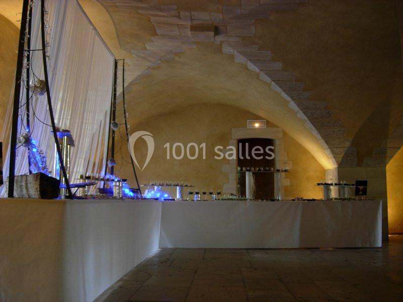 Salle voûtée éclairée avec une grande table décorée de lumières bleues et disposée pour un événement.