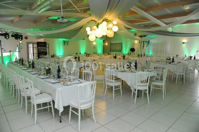 Salle de réception décorée avec des tables dressées, des chaises blanches et un éclairage vert et blanc.