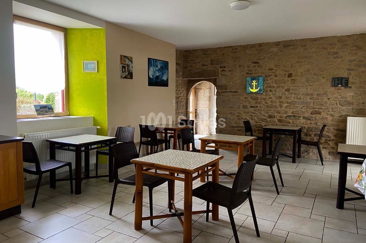 Salle à manger lumineuse avec murs en pierre, tables en bois, chaises noires et une fenêtre donnant sur l'extérieur.