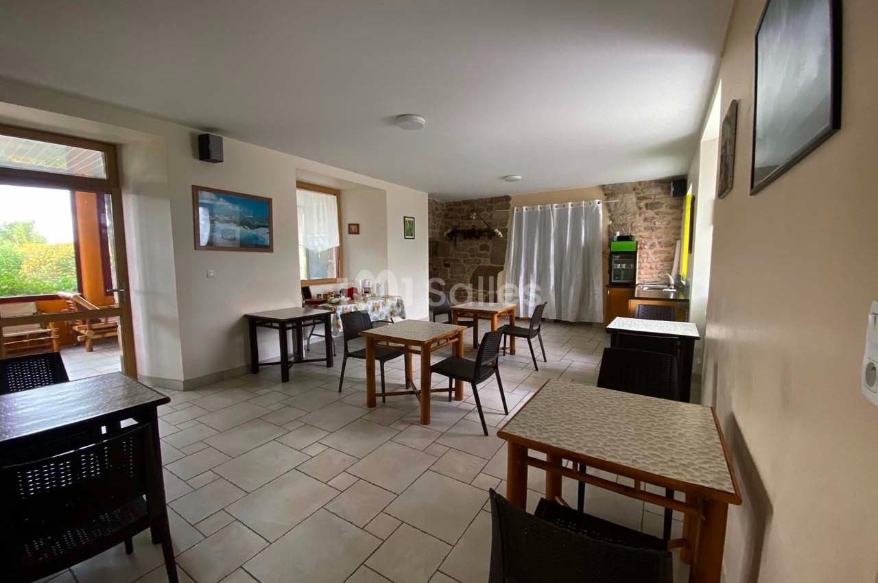 Salle à manger lumineuse avec tables en bois espacées, murs clairs et une baie vitrée donnant sur l'extérieur.