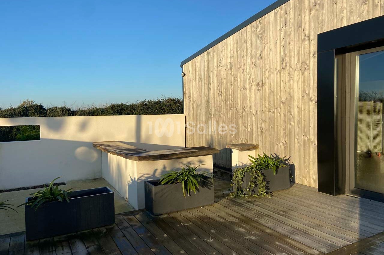 Terrasse en bois avec jardinières, bancs intégrés et façade en bois clair sous un ciel dégagé.
