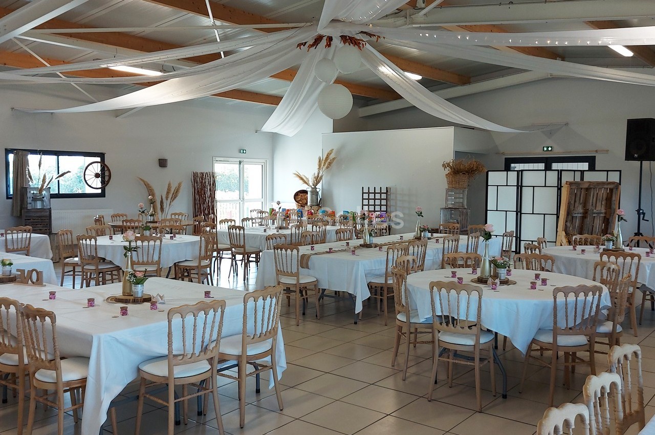 Salle de réception décorée avec des tables rondes dressées, nappes blanches et éléments décoratifs suspendus.