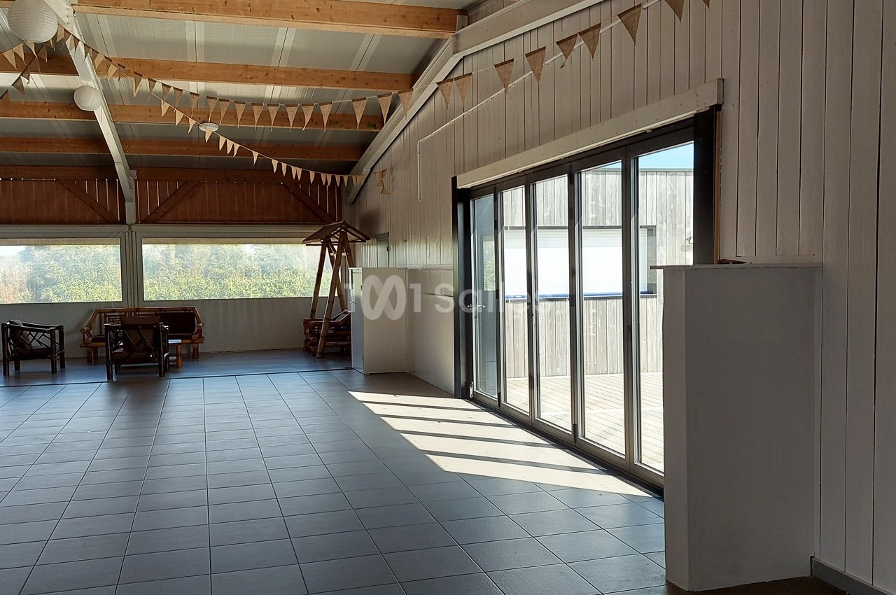 Salle lumineuse avec carrelage gris, grandes baies vitrées, plafond en bois et guirlandes décoratives suspendues.