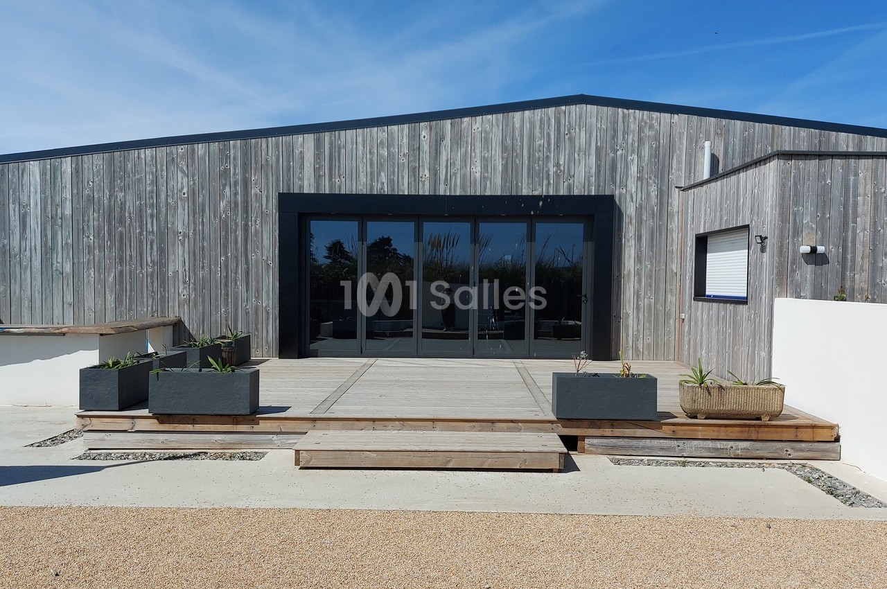 Façade d'un bâtiment moderne en bois avec une terrasse en béton, des jardinières et un ciel dégagé en arrière-plan.
