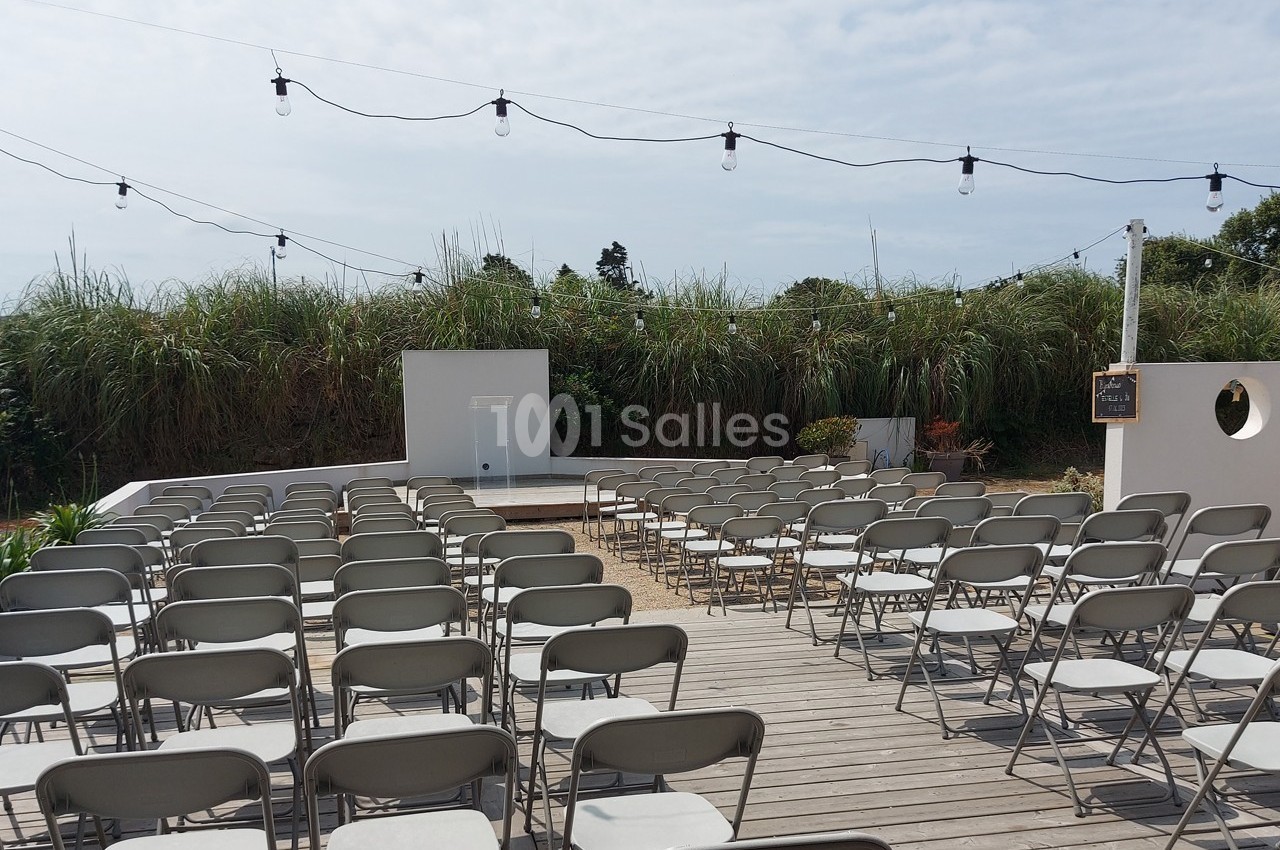 Chaises pliantes alignées sur une terrasse en bois, face à un écran blanc en extérieur, sous des guirlandes lumineuses.